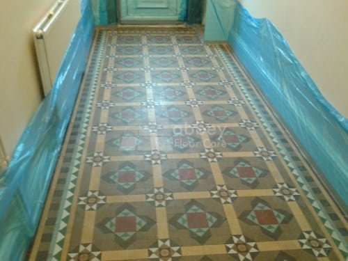 Close-up of stained Victorian Minton tiles with patchy surface finish before restoration