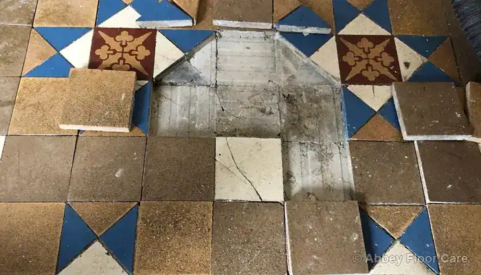 Loose Victorian floor tiles lifted from fractured lime screed beneath the surface
