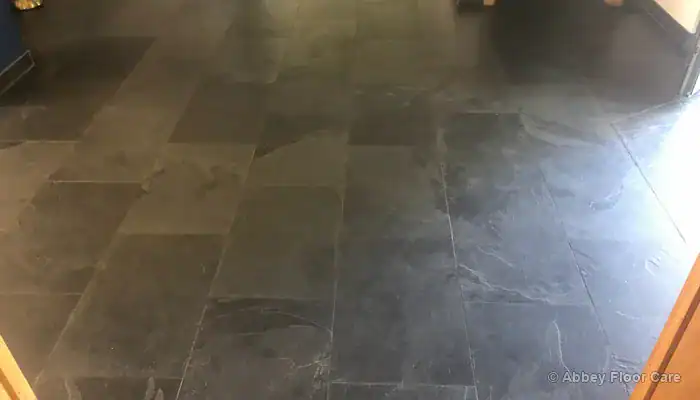 Thick buildup of discoloured floor wax accumulated along slate tile edges and grout