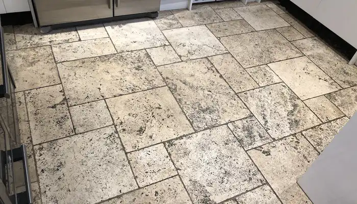 Travertine floor exhibiting darkened patches, worn finish, and uneven surface tone