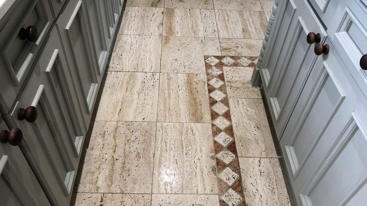Worn travertine kitchen floor exhibiting dull traffic areas and natural colour variation