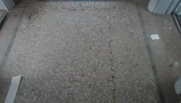 Terrazzo hallway floor with dark adhesive staining before restoration